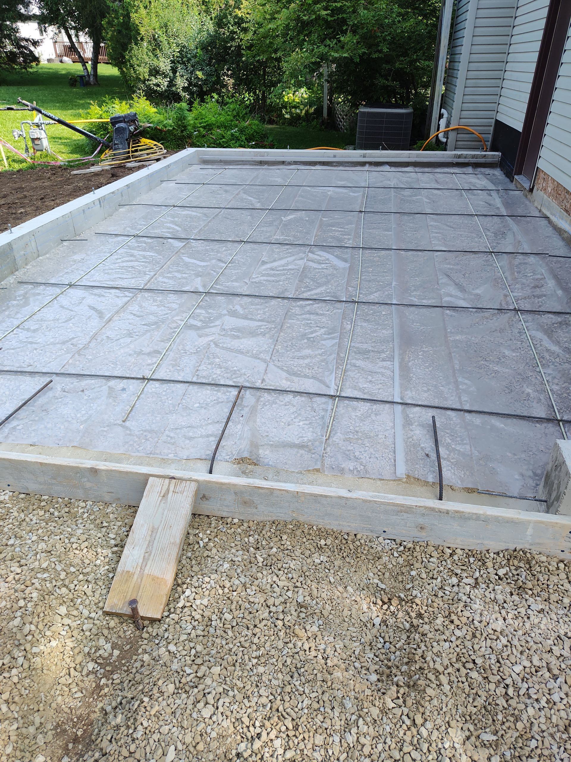 Raised gray patio slabs beside a house, with a gravel edge and green yard in the background
