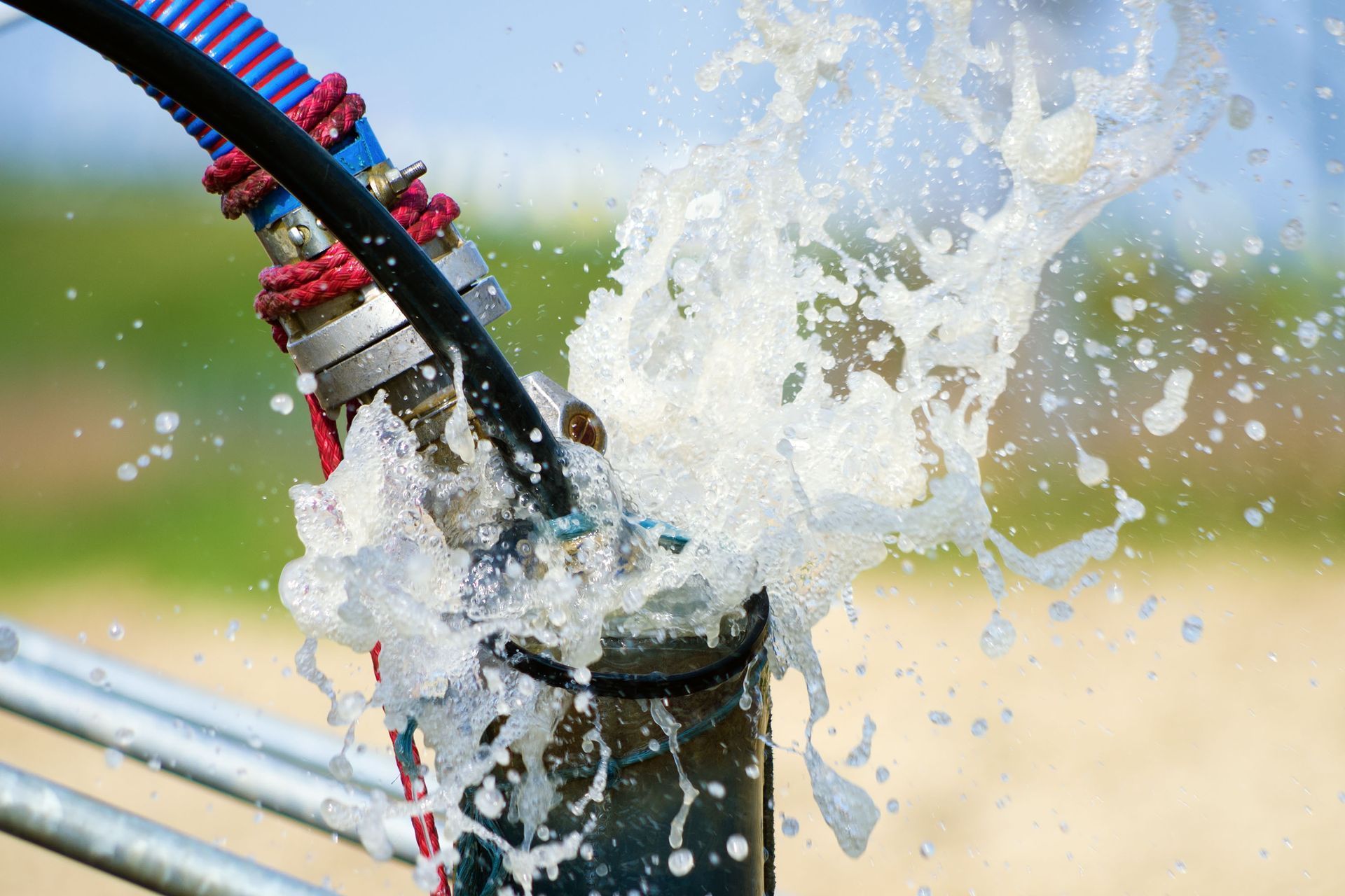 Water gushing from a pipe connected to a blue and black hose, outdoors.