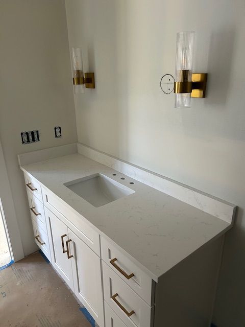 White bathroom vanity with gold hardware, countertop, and sconces.
