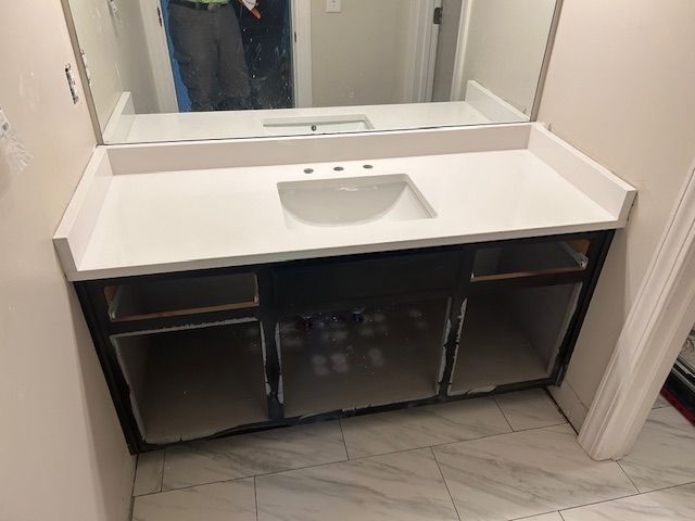 Bathroom vanity with white countertop, sink, and mirror. Dark cabinetry with open storage, unfinished.