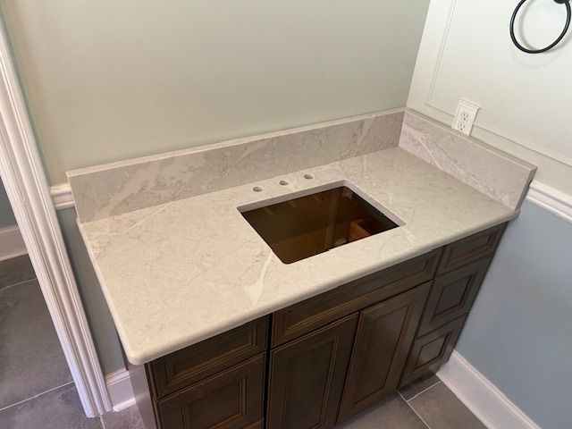 Vanity with light-colored countertop, bronze sink, and dark wood cabinets in a bathroom.