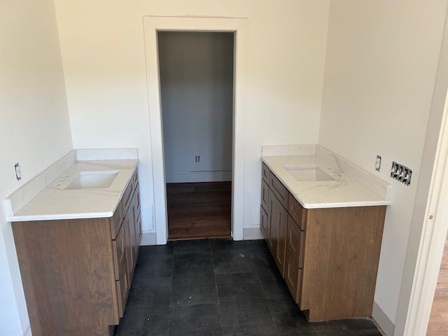 Two brown bathroom vanities with white countertops flanking a doorway, dark tiled floor.