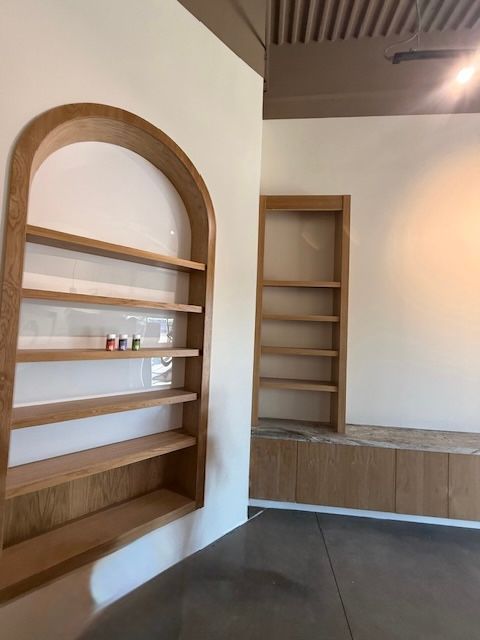 Wooden built-in shelving units in a neutral-colored room with exposed concrete flooring.