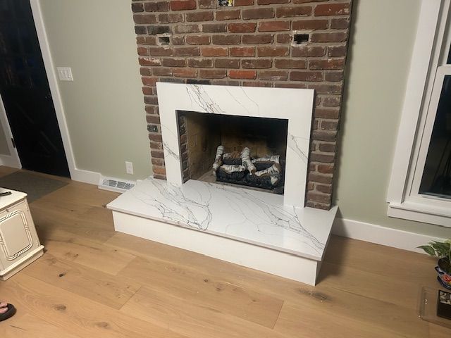 Fireplace with marble surround and hearth, set against brick and light green wall.