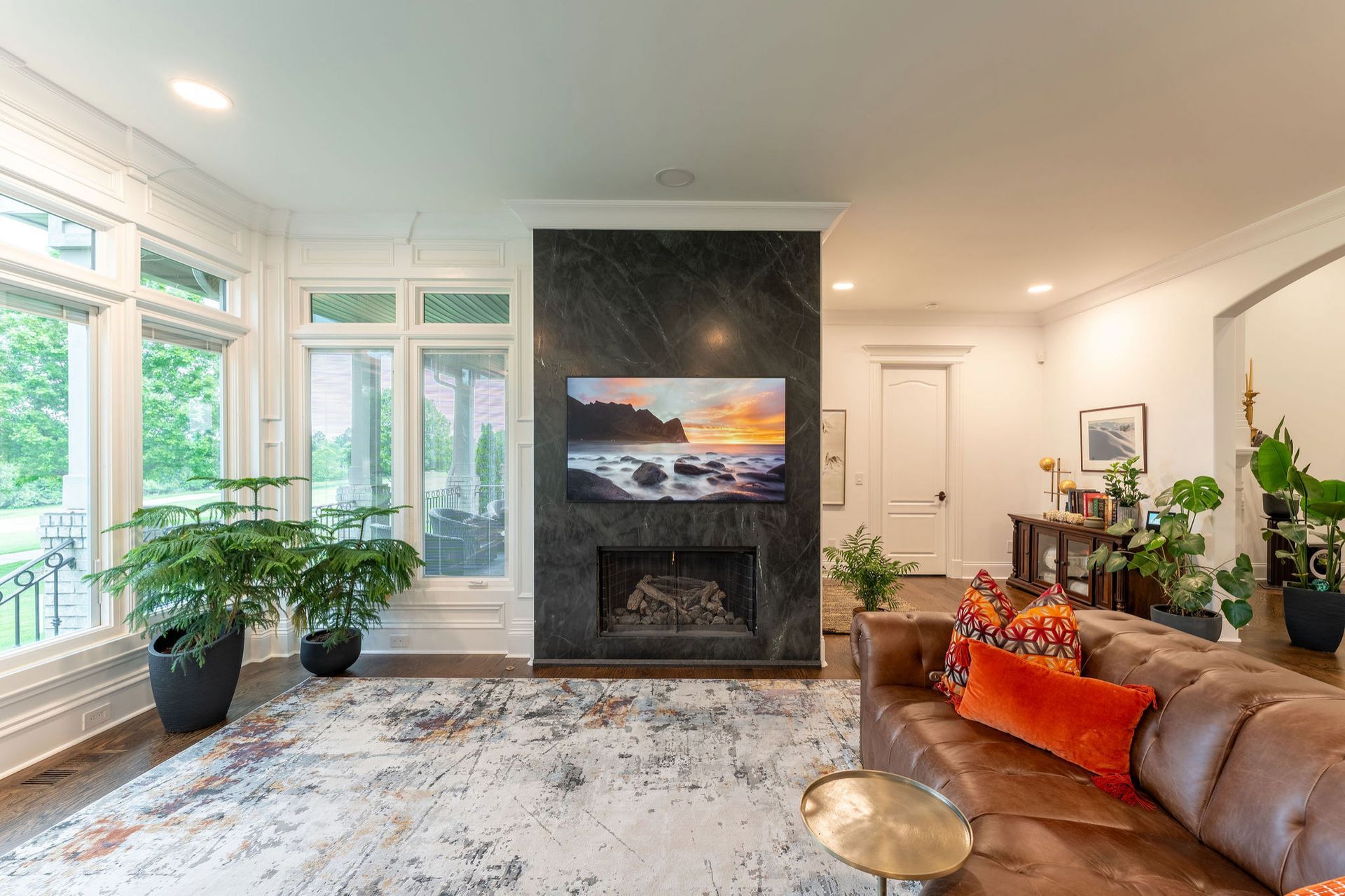 Living room with fireplace, TV, leather sofa, and large windows.