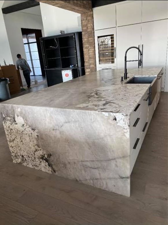 Kitchen island with light-colored granite countertop, black faucet, white cabinets, and a man in the background.