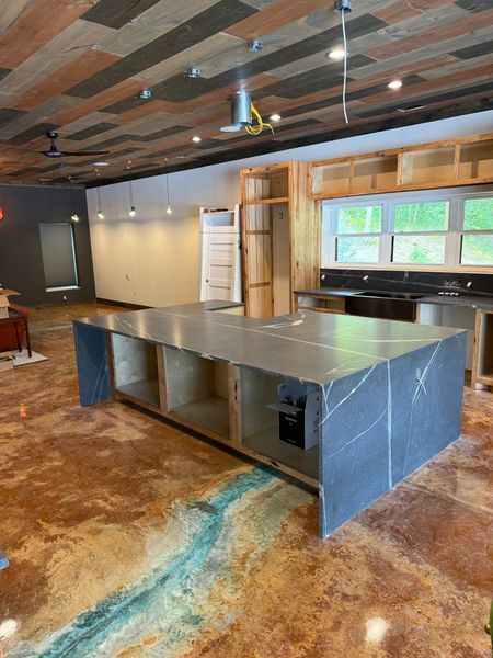 Kitchen under construction with island, cabinets, stone countertops, and stained concrete floor.