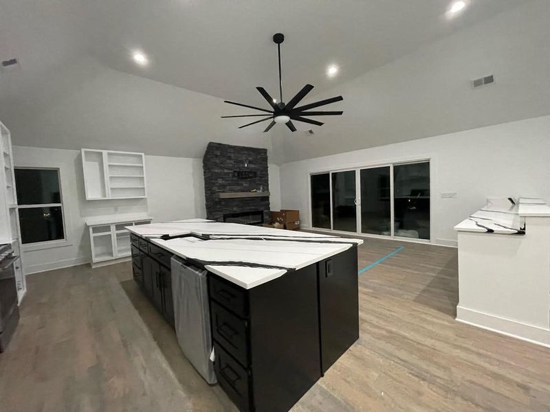 Modern kitchen with large island, fireplace, and glass doors. Black cabinets, white countertops, wood floor.