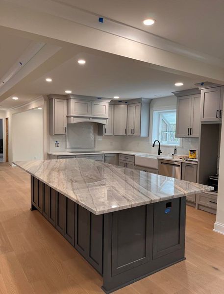 Kitchen with gray cabinets, a dark gray island with a light-colored countertop, and light wood floors.