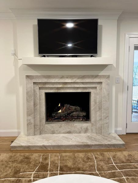 Fireplace with TV mounted above, white marble facade, lit fire in the center, and wood flooring.