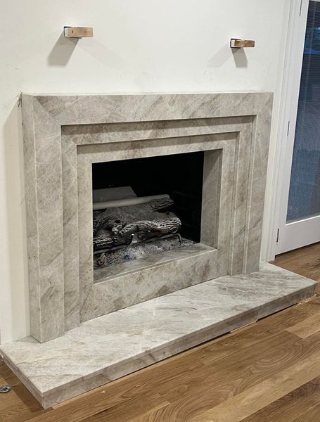 A marble fireplace with a recessed firebox and decorative trim, set against a white wall.