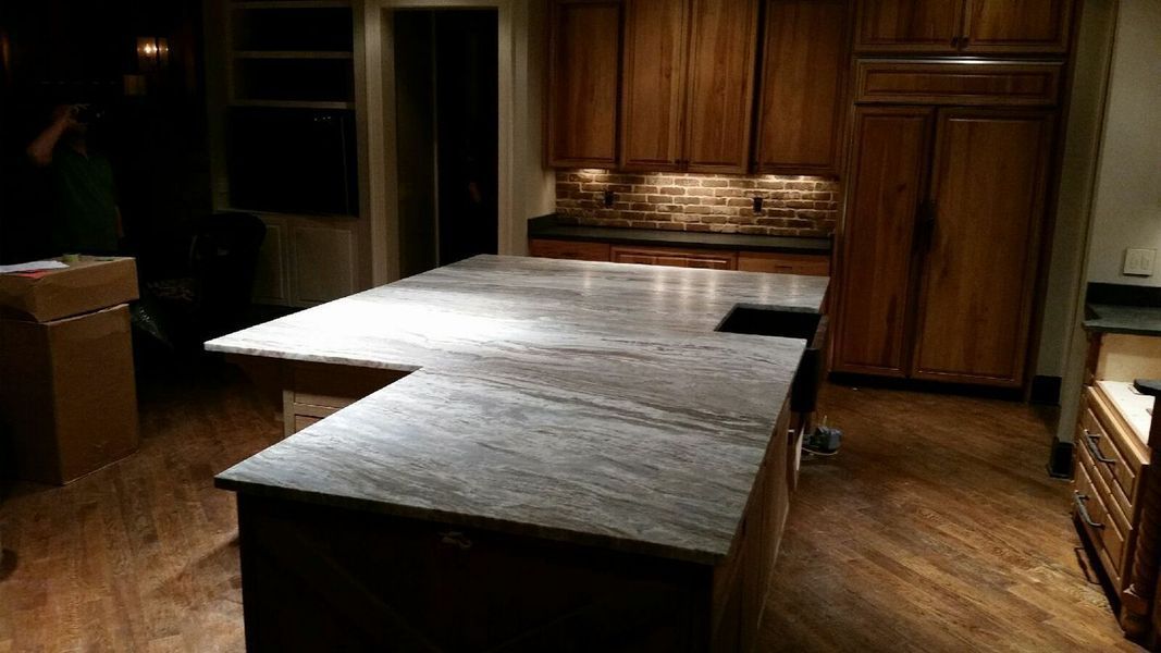 Kitchen with large gray countertop island, dark wooden cabinets, and wood flooring.