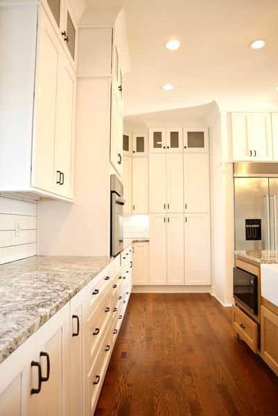 Bright white kitchen with granite countertops, wood floors, and stainless steel appliances.