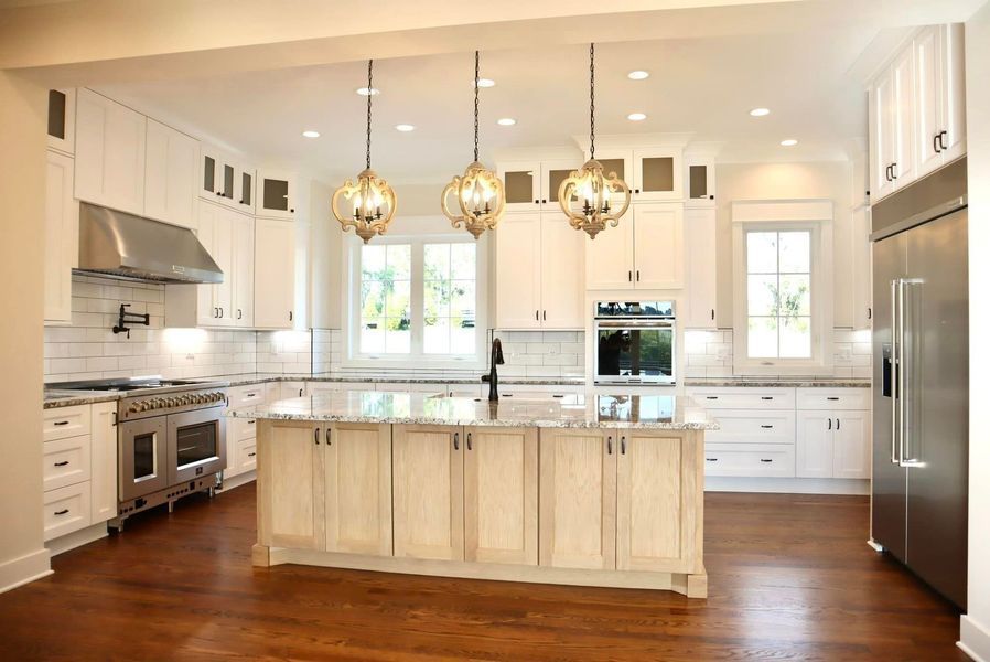 Bright white kitchen with a large island, stainless steel appliances, and wood floors.