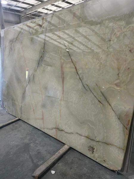 Large slab of polished green marble with dark veining, leaning against a wall indoors.