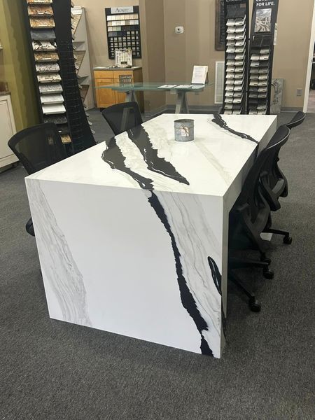 White countertop with black veining, surrounded by black chairs in a showroom.