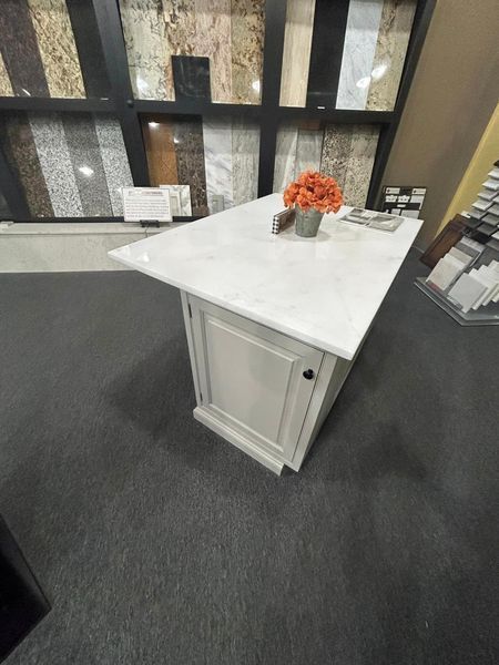 White countertop on a white cabinet with a flower arrangement, showroom setting with stone samples.