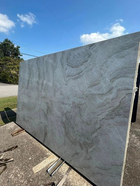 Large rectangular slab of light gray stone with swirling patterns, outdoors under a blue sky.