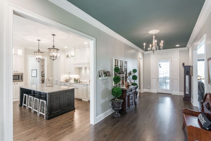 Hallway with dark wood floor, leading to a kitchen with a dark island, and a front door. Teal ceiling.