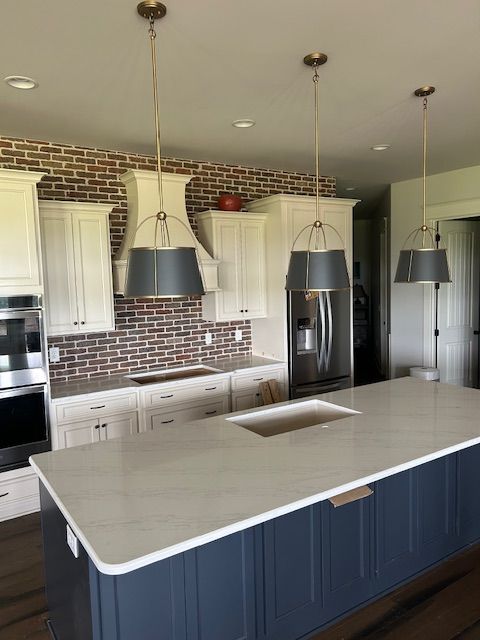 Kitchen with white cabinets, blue island, brick backsplash, and three gray pendant lights.
