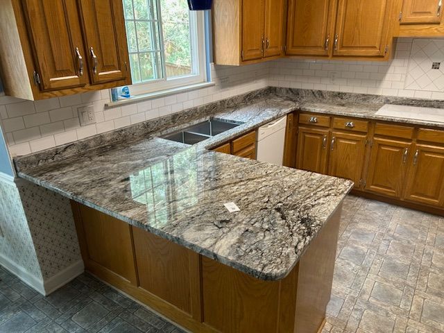 A remodeled kitchen with wooden cabinets, gray countertops, and a white backsplash.