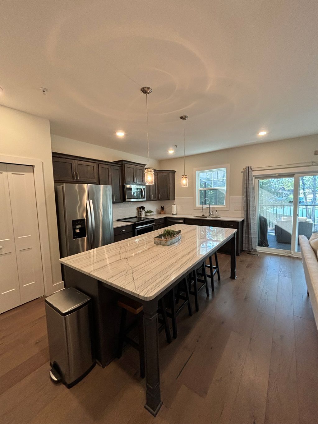 Modern kitchen with large island, stainless steel appliances, dark cabinets, and hardwood floors.
