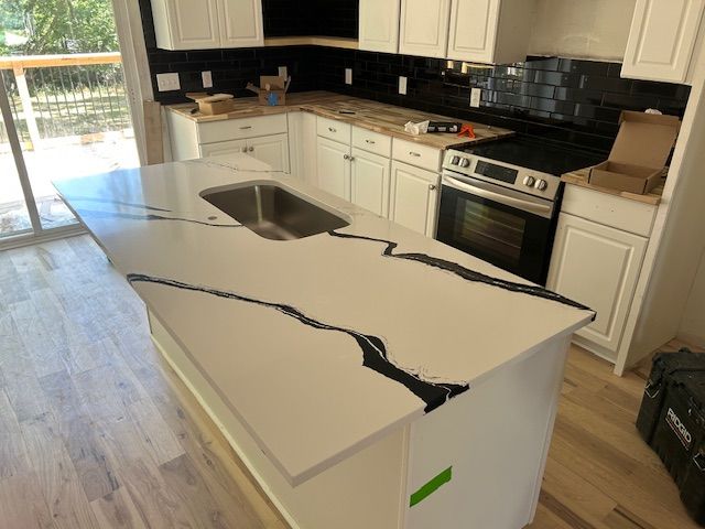 White kitchen with quartz countertops and black veining, stainless steel oven, and black tile backsplash.