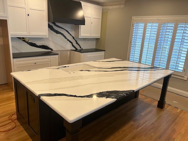 Kitchen with white cabinets, black countertops and island, and wooden flooring.