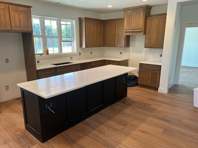 Kitchen with brown cabinets, black island, white countertops, and wood floors.