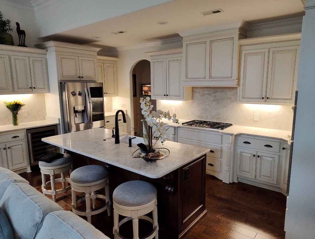 A kitchen with distressed white cabinets, dark island, and a stainless steel refrigerator.