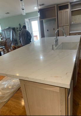 Kitchen island with light-colored countertop, cabinets, and a sink. A person stands near a door.
