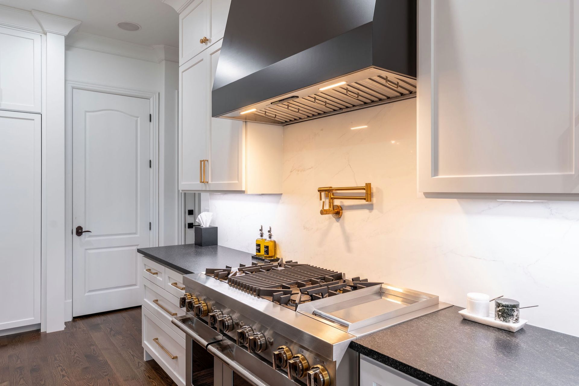 Modern kitchen with stainless steel stove, black hood, white cabinets, and dark countertop.