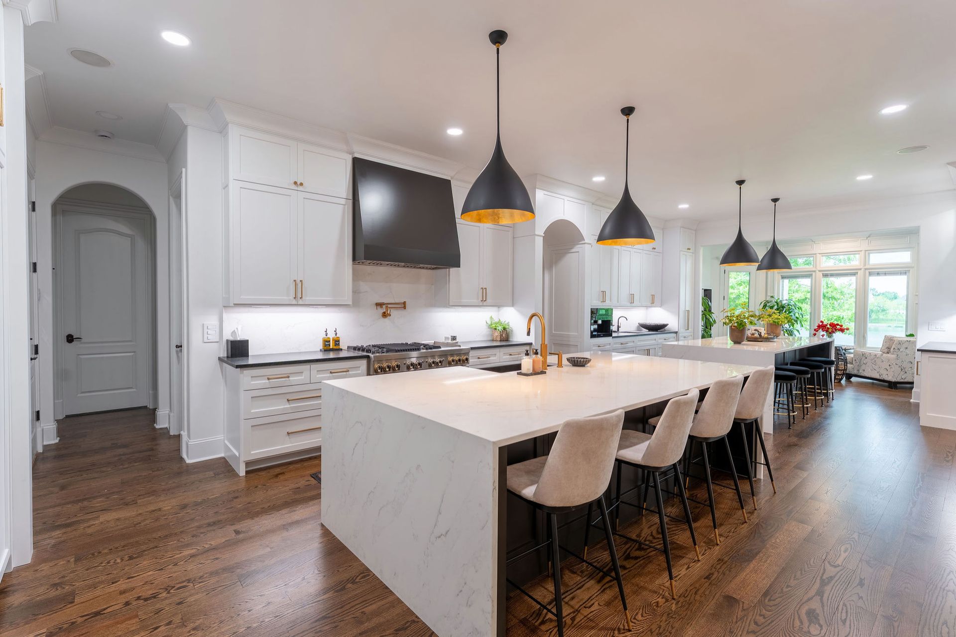 Spacious white kitchen with island, pendant lights, bar stools, and dark wood floors.