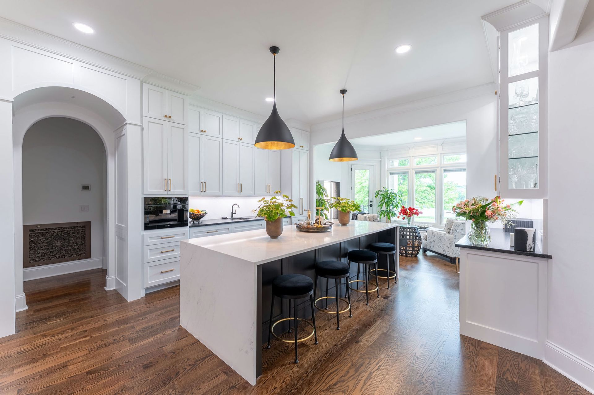 Kitchen with white cabinets, dark island, gold pendant lights, and hardwood floors.