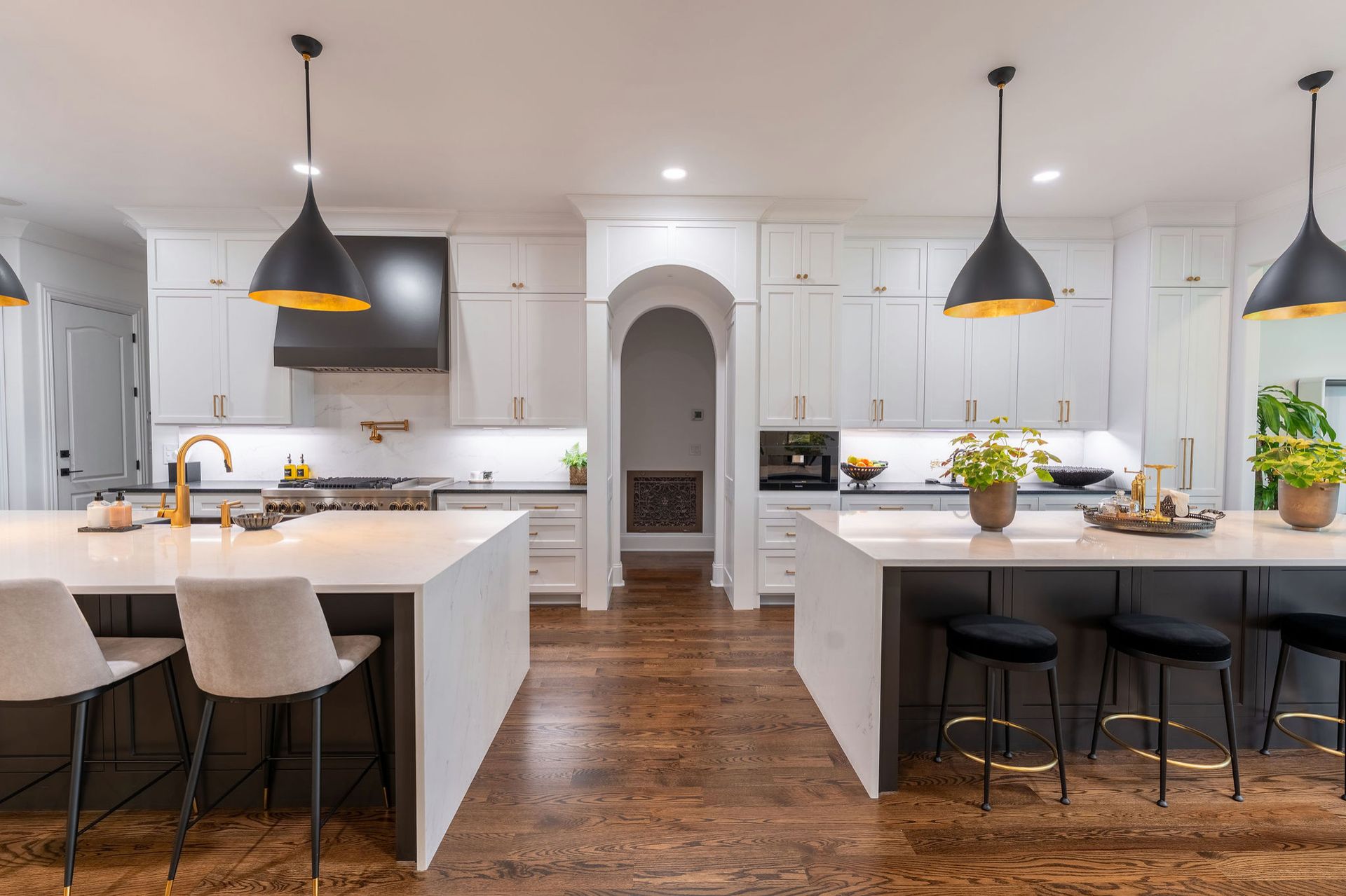 Modern kitchen with two islands, white cabinets, black pendant lights, and wooden floors.