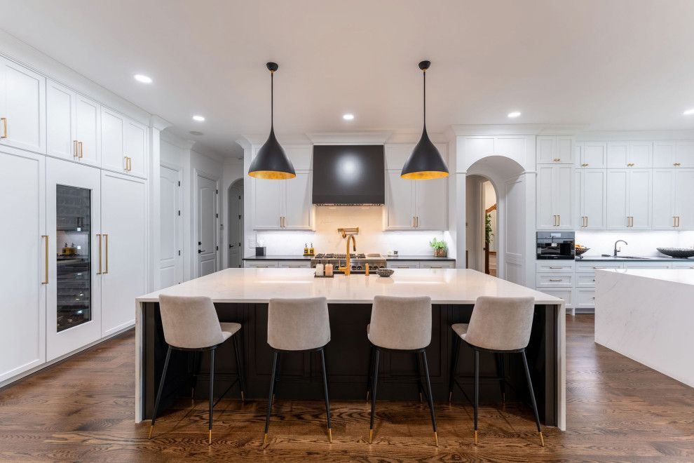 Modern white kitchen with dark island and gold accents; bar seating.
