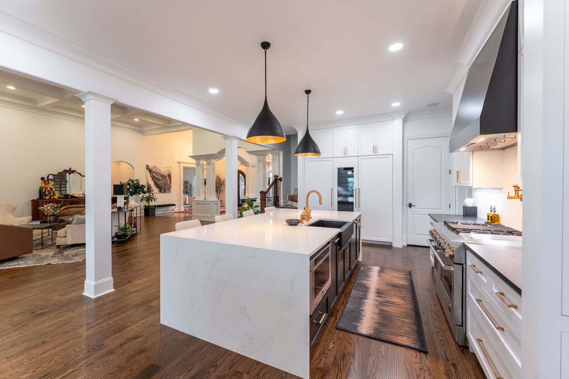 Modern kitchen with white island, dark cabinets, and pendant lights. Open concept to living room.