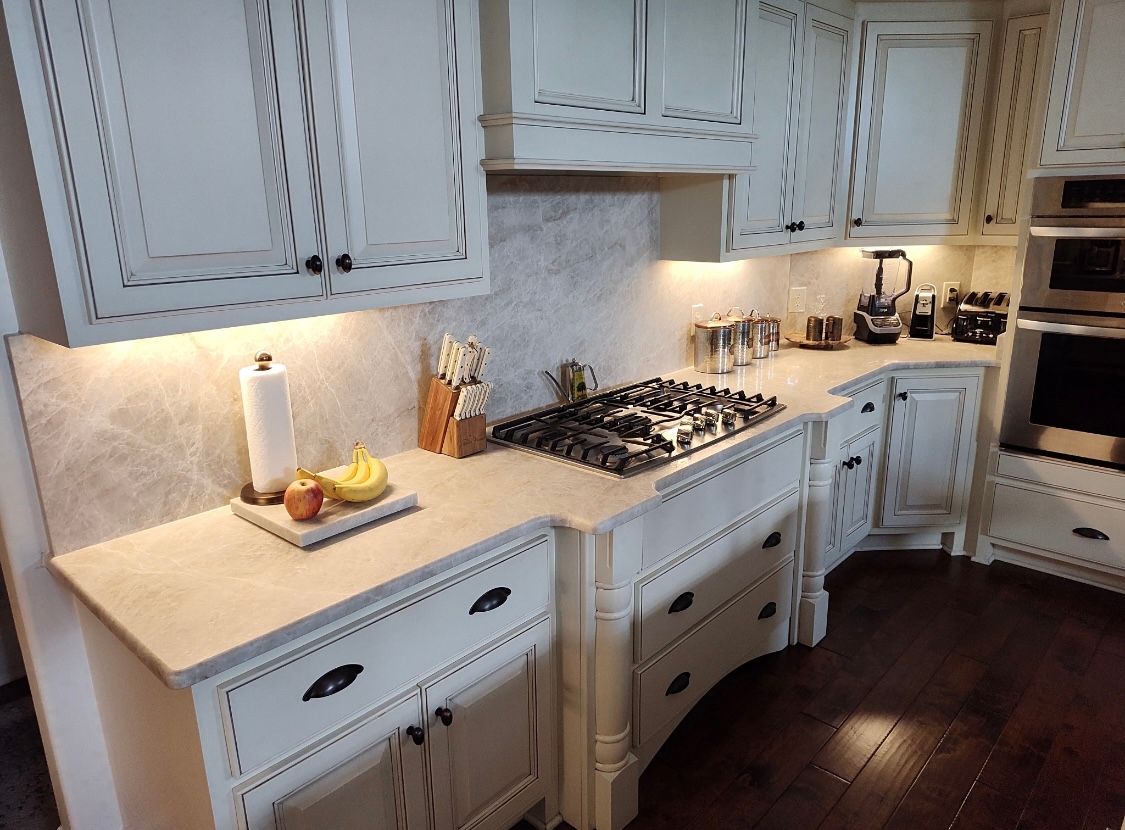 Kitchen with off-white cabinets, marble backsplash, gas stovetop, and dark wood floors.