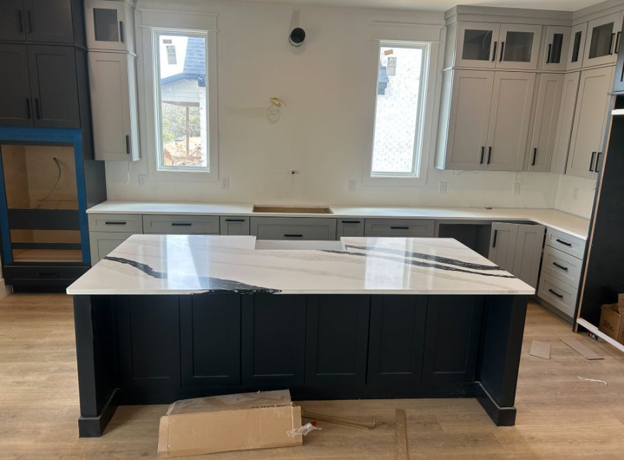 Kitchen with dark blue island and light gray countertops/cabinets, wood floors, two windows.