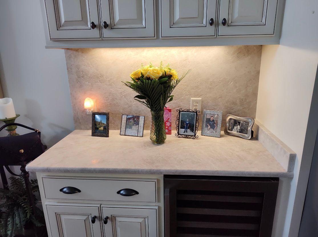 A cabinet with a flower bouquet, framed photos, and a lit candle. White cabinets above.