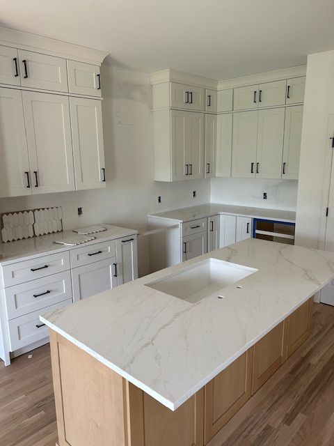 White kitchen cabinets with black handles, light countertops, and wooden island in a room.