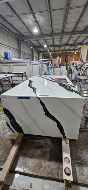 A large white countertop with black veining sits on a wooden frame inside a workshop.