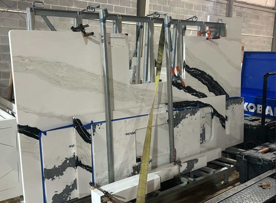 Slabs of white and gray patterned stone are clamped to a metal rack in a workshop, ready for cutting.