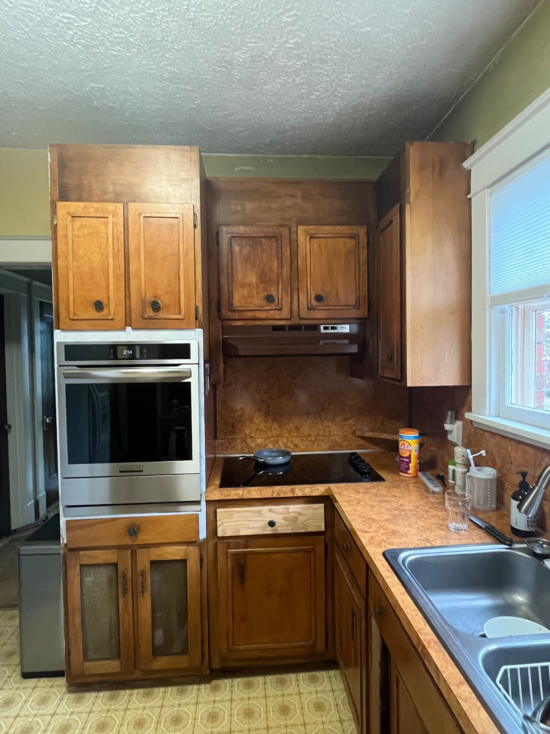 Kitchen with wooden cabinets, built-in oven, stovetop, and sink. Brown and yellow tones dominate. 