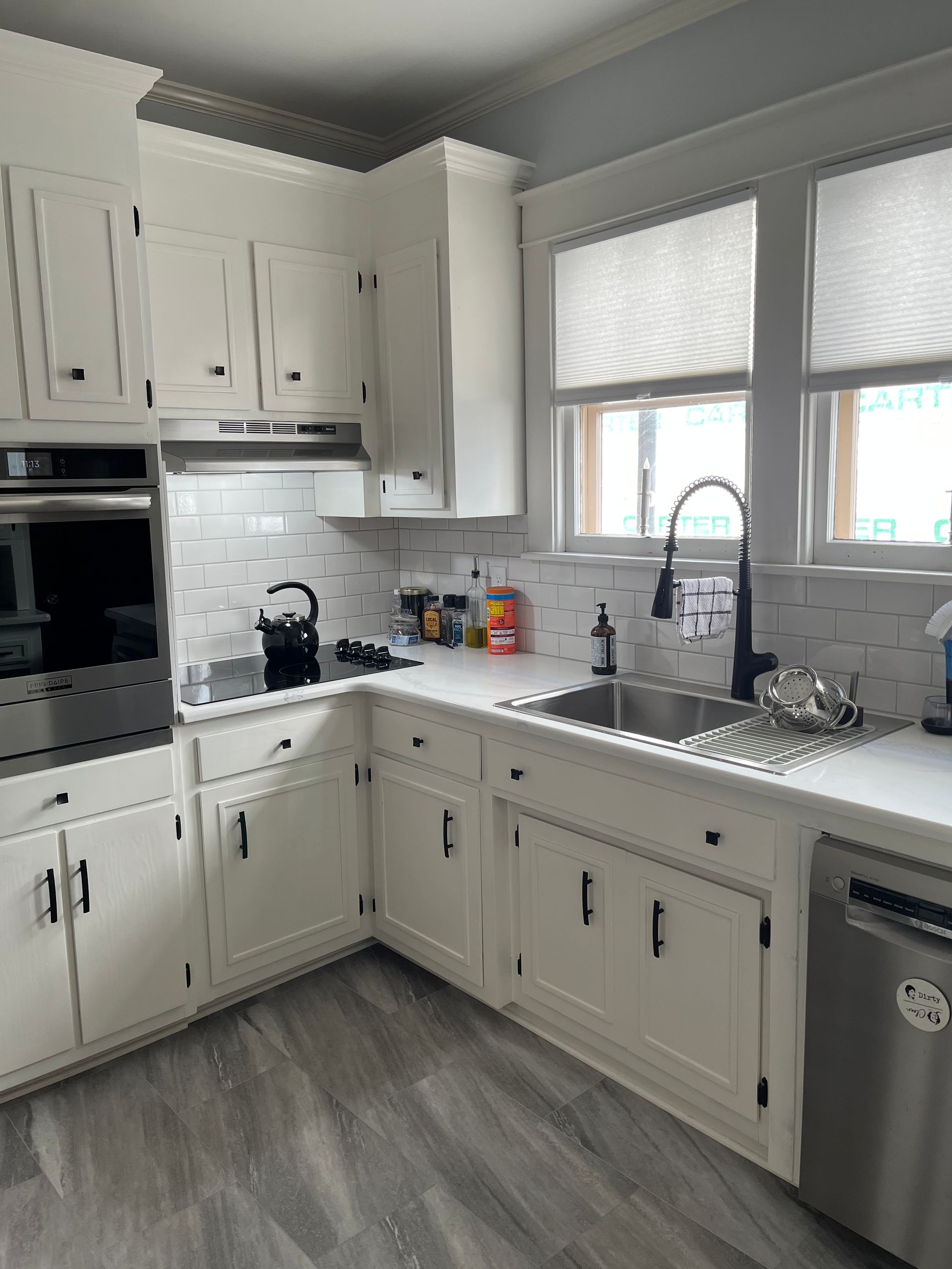 White kitchen with stainless steel appliances, white cabinets, and dark hardware. 
