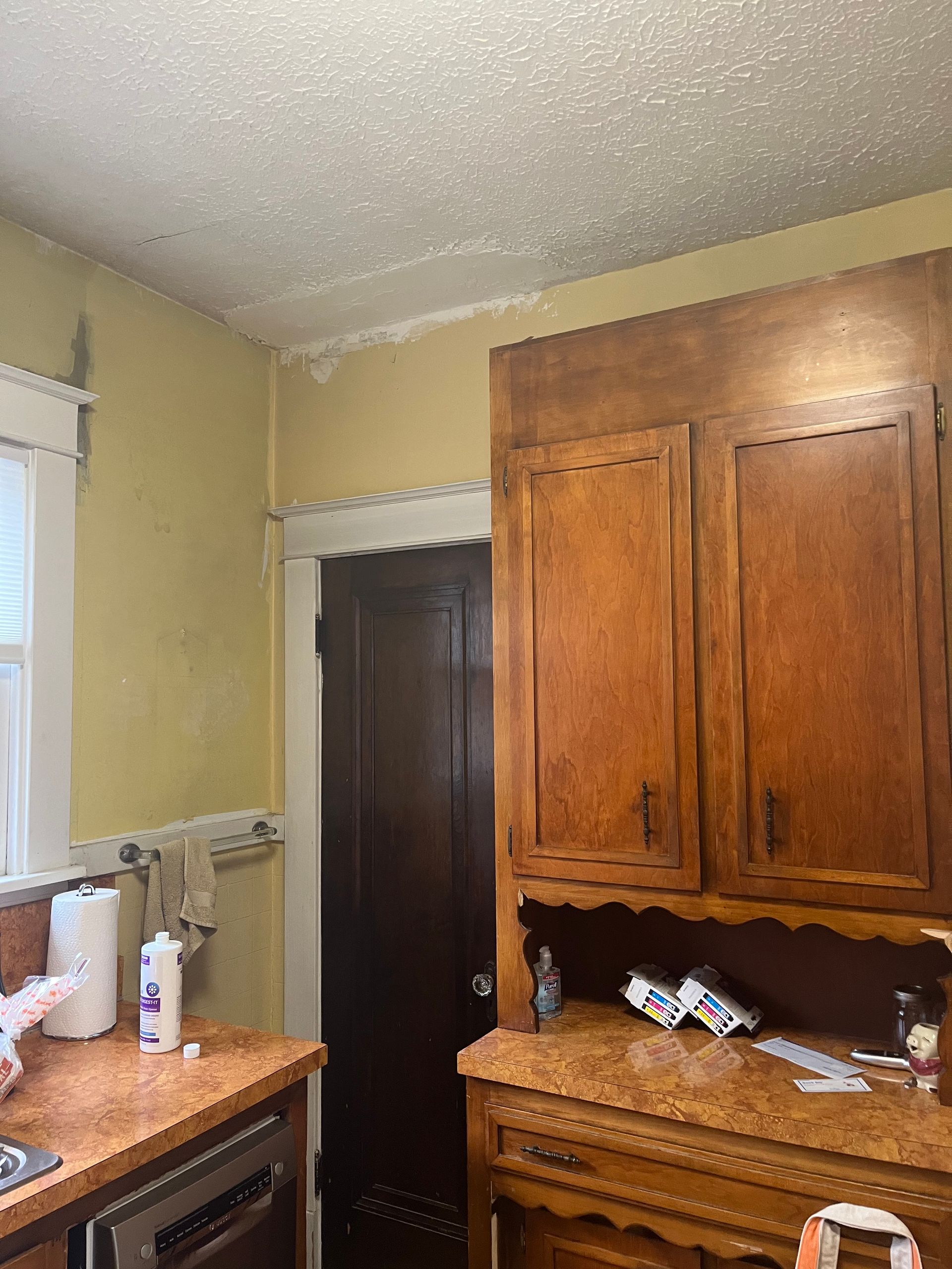Kitchen corner with yellow walls, dark cabinets, and water damage on the ceiling. 