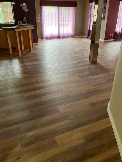 Hardwood-like flooring in a room with purple curtains and walls. A small kitchen area is visible in the background.