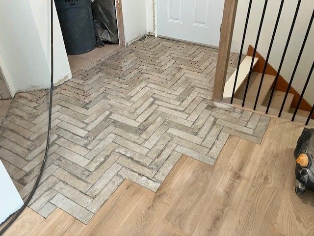 Herringbone tile and wood flooring installation in a doorway, partially complete.
