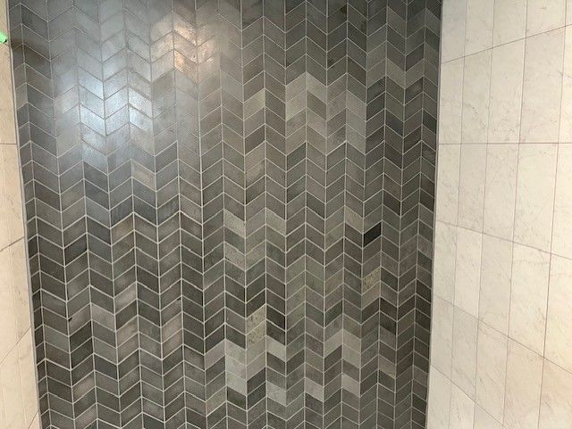 Gray herringbone tile wall next to a white marble wall.