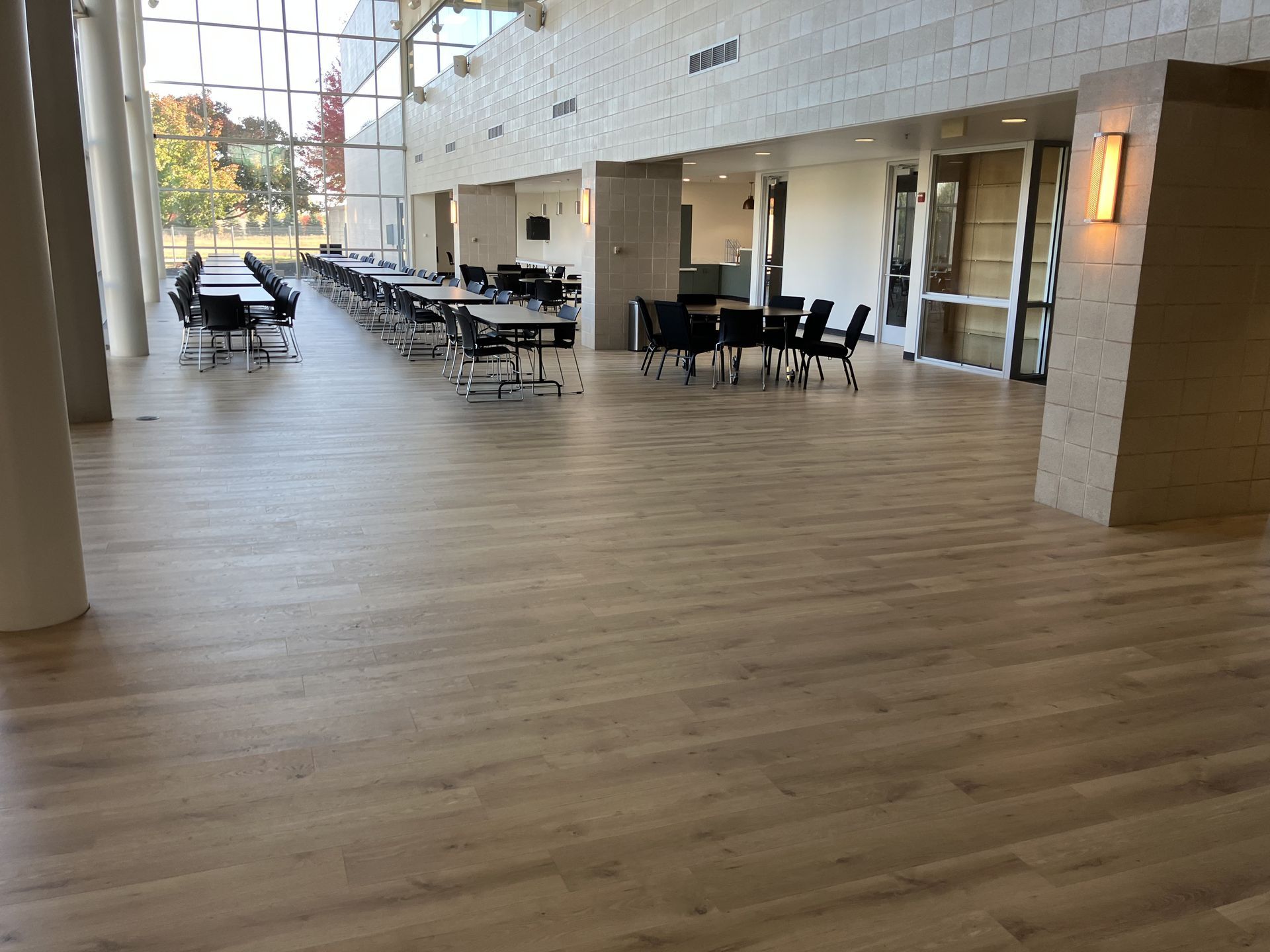 Light-colored, open room with tables and chairs. Large windows on left, stone walls on right.